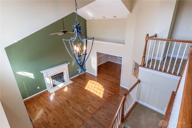 stairway featuring wood finished floors, baseboards, a premium fireplace, a towering ceiling, and a chandelier