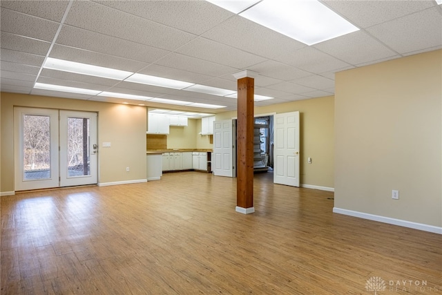 unfurnished living room with a paneled ceiling, baseboards, and light wood-style floors