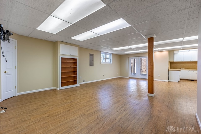 basement with a drop ceiling, baseboards, and light wood-style floors
