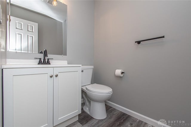 bathroom featuring baseboards, toilet, wood finished floors, and vanity