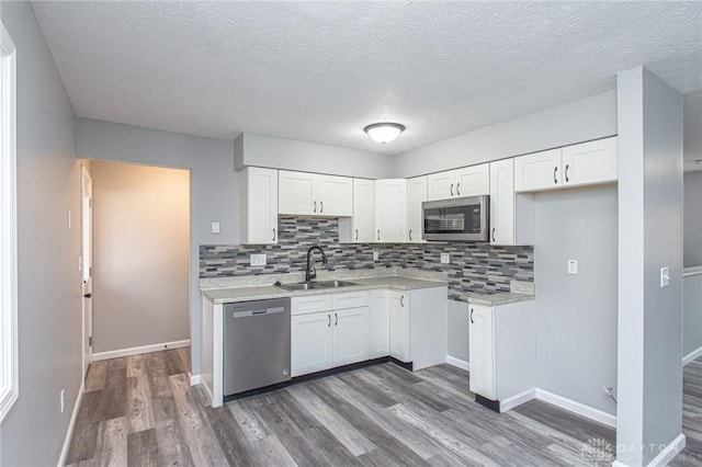 kitchen with a sink, stainless steel appliances, wood finished floors, and white cabinetry