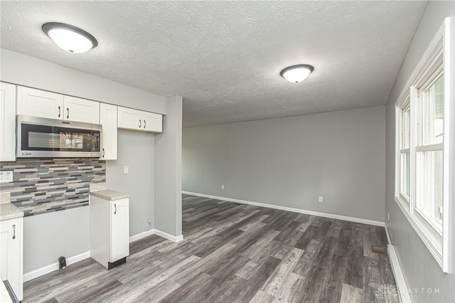 kitchen featuring stainless steel microwave, light countertops, decorative backsplash, dark wood-style floors, and white cabinets