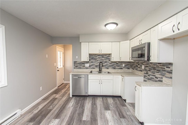 kitchen with a baseboard radiator, light countertops, wood finished floors, stainless steel appliances, and a sink