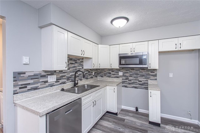 kitchen with a sink, white cabinetry, stainless steel appliances, light countertops, and dark wood-style flooring