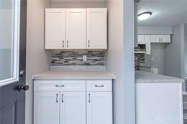 kitchen featuring stainless steel microwave, white cabinets, light countertops, and tasteful backsplash