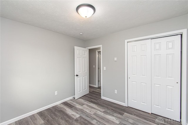 unfurnished bedroom featuring a closet, a textured ceiling, baseboards, and wood finished floors