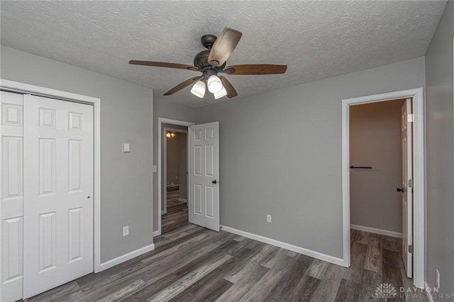 unfurnished bedroom with a closet, a textured ceiling, dark wood-type flooring, and baseboards