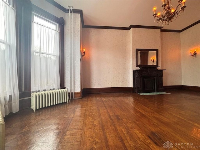 unfurnished living room with radiator, wood finished floors, baseboards, ornamental molding, and a notable chandelier