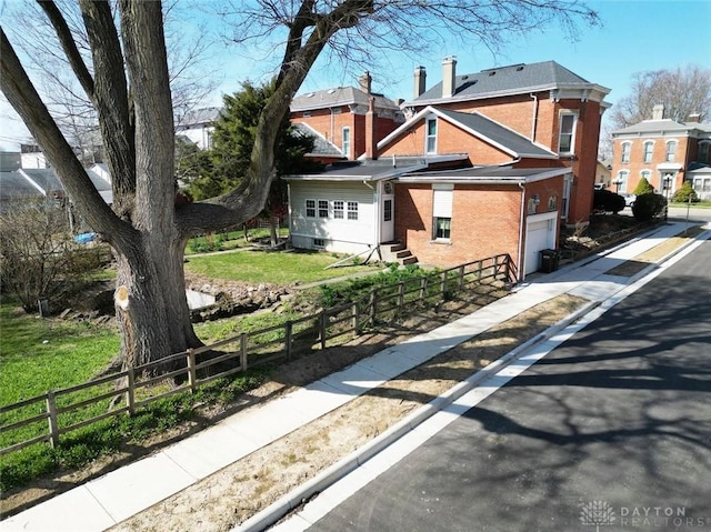 view of side of home featuring brick siding, a fenced front yard, entry steps, driveway, and an attached garage