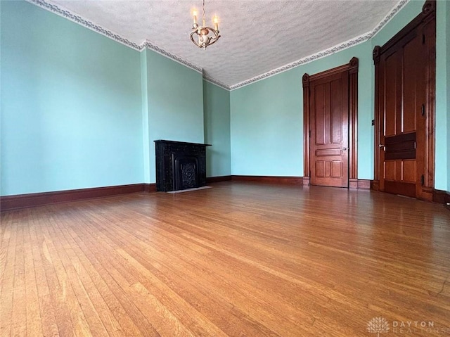 unfurnished living room featuring baseboards, a chandelier, ornamental molding, wood finished floors, and a textured ceiling