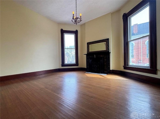 unfurnished living room with hardwood / wood-style floors, baseboards, an inviting chandelier, a fireplace with flush hearth, and a textured ceiling