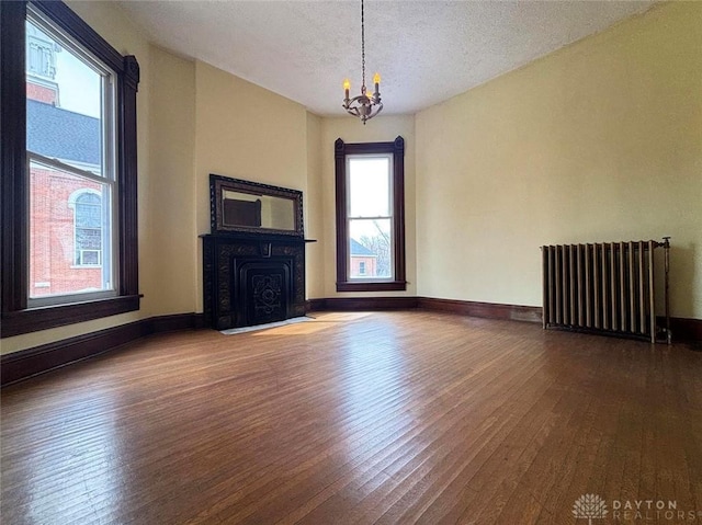 unfurnished living room featuring radiator, baseboards, an inviting chandelier, and hardwood / wood-style flooring
