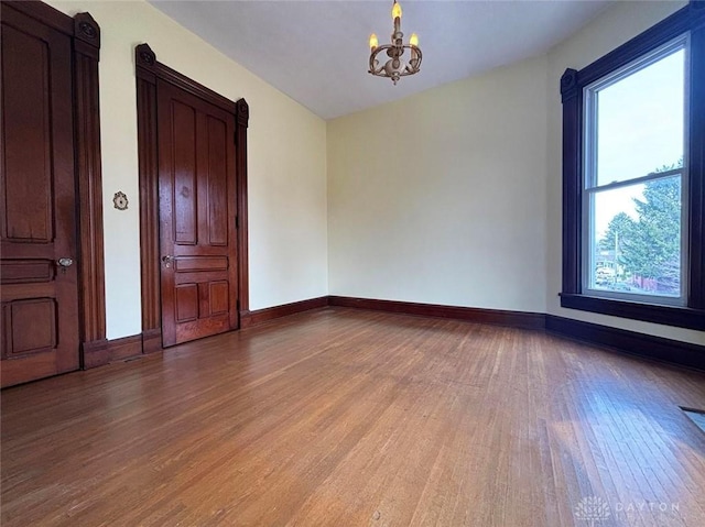 empty room featuring a notable chandelier, baseboards, and light wood-type flooring