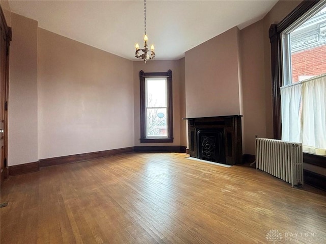 unfurnished living room with a fireplace with flush hearth, wood finished floors, radiator, baseboards, and a chandelier
