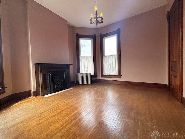 unfurnished living room with hardwood / wood-style floors, a notable chandelier, radiator heating unit, and baseboards