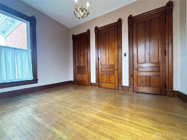 unfurnished bedroom with baseboards, a notable chandelier, and light wood-style flooring