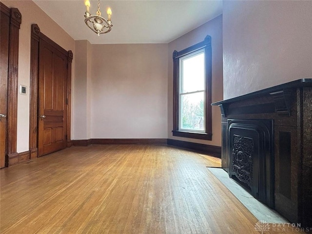 unfurnished living room featuring baseboards, an inviting chandelier, light wood-style flooring, and a fireplace with flush hearth