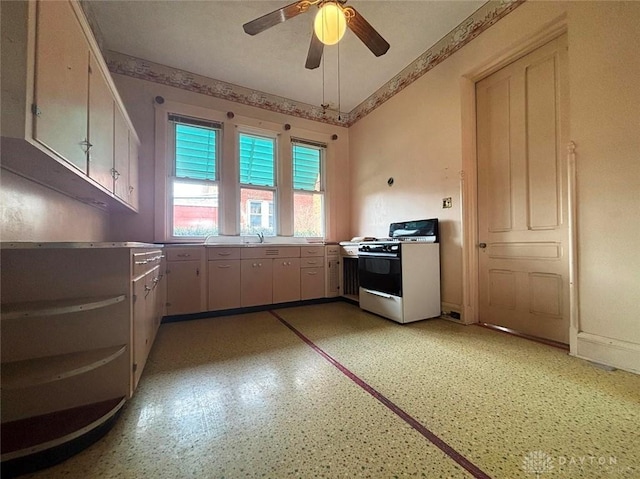 kitchen with a sink, ceiling fan, gas range oven, and light countertops