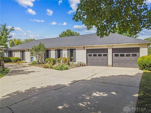 ranch-style home featuring roof with shingles, an attached garage, driveway, and brick siding