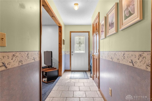doorway with light tile patterned floors and a wainscoted wall