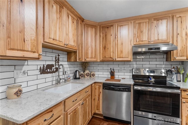 kitchen featuring backsplash, appliances with stainless steel finishes, light stone countertops, a sink, and under cabinet range hood