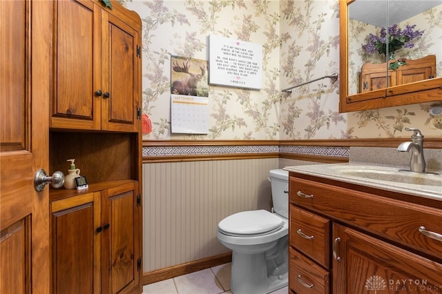 bathroom featuring tile patterned flooring, vanity, wainscoting, toilet, and wallpapered walls