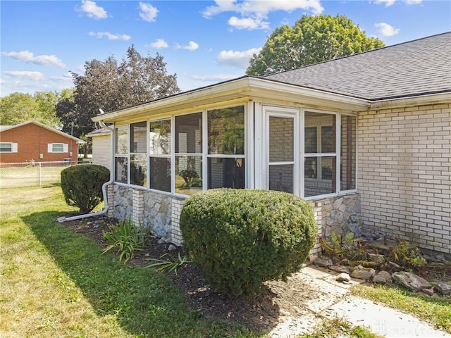 view of home's exterior with a sunroom, brick siding, fence, a yard, and a shingled roof