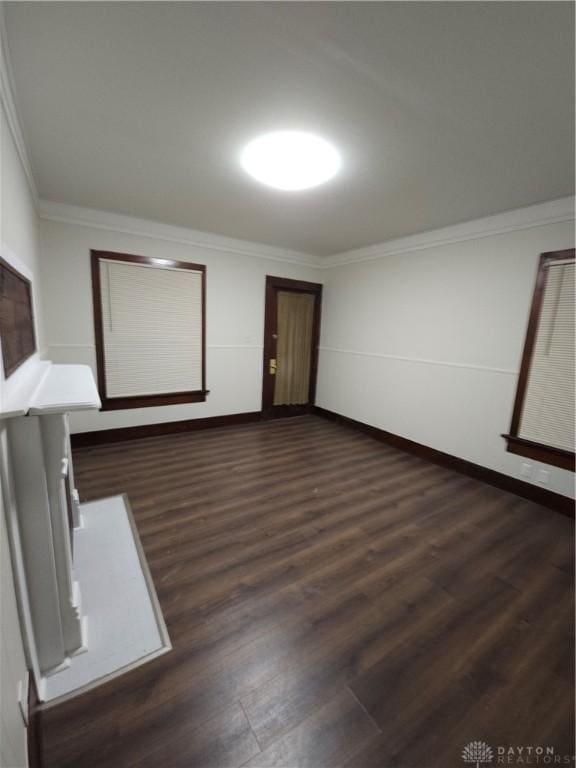 empty room with baseboards, crown molding, and dark wood finished floors