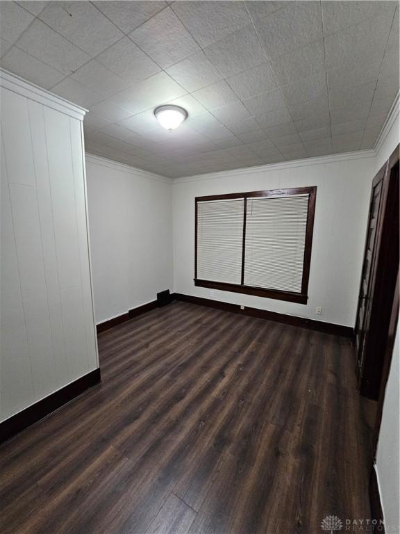 spare room with crown molding, baseboards, and dark wood finished floors