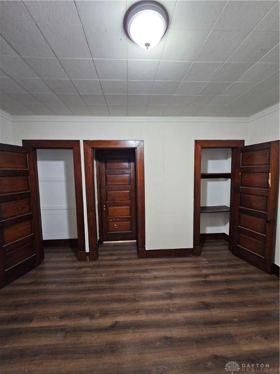 unfurnished bedroom featuring ornamental molding, baseboards, and dark wood-style floors