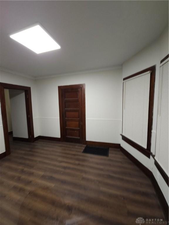 empty room featuring dark wood-type flooring, baseboards, and crown molding