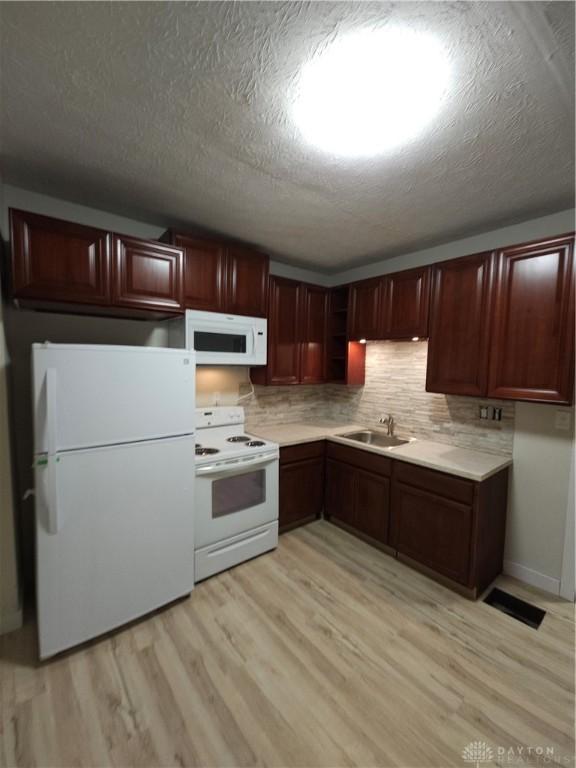 kitchen featuring white appliances, light countertops, backsplash, light wood-style floors, and a sink