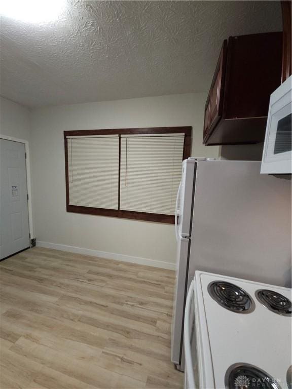 kitchen featuring white appliances, light wood-style floors, a textured ceiling, and baseboards