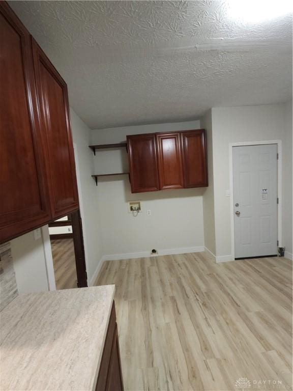 laundry room with light wood-style flooring, a textured ceiling, washer hookup, baseboards, and cabinet space