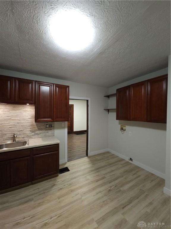 kitchen featuring tasteful backsplash, baseboards, a sink, light countertops, and light wood-style floors