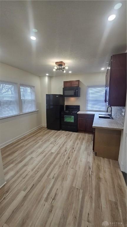 kitchen featuring light wood-style flooring, black appliances, a sink, light countertops, and baseboards