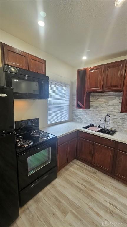 kitchen with light wood-type flooring, tasteful backsplash, black appliances, light countertops, and a sink