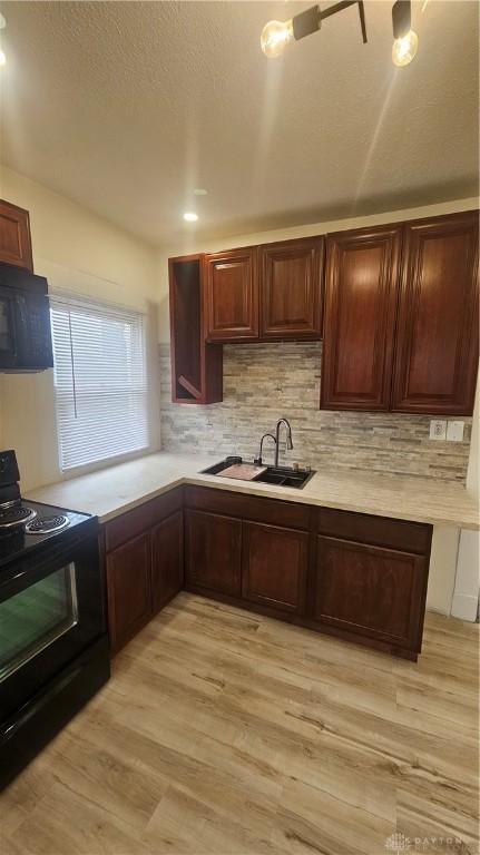 kitchen featuring light wood-type flooring, tasteful backsplash, black appliances, light countertops, and a sink
