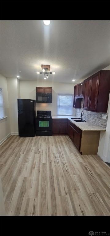 kitchen with a sink, light countertops, black appliances, and light wood finished floors