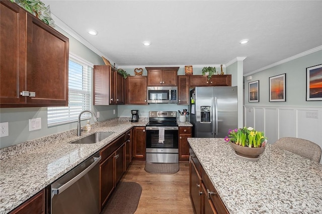 kitchen with light stone counters, wood finished floors, a sink, appliances with stainless steel finishes, and ornamental molding