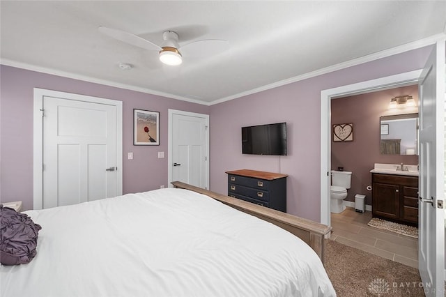 tiled bedroom featuring a ceiling fan, crown molding, a sink, baseboards, and ensuite bath