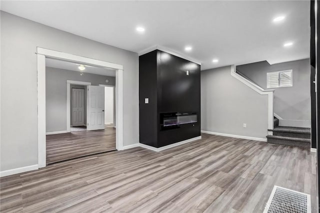 unfurnished living room with stairway, recessed lighting, wood finished floors, and baseboards