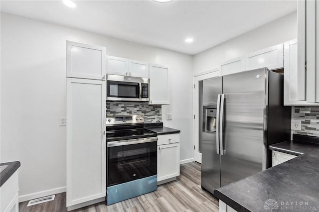 kitchen with baseboards, light wood finished floors, stainless steel appliances, white cabinets, and dark countertops