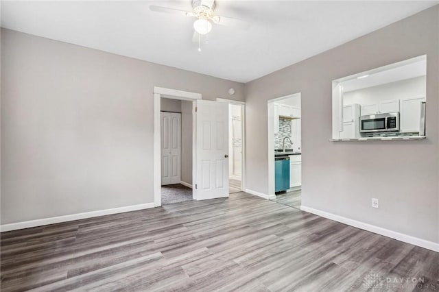 unfurnished bedroom featuring a ceiling fan, baseboards, a sink, light wood-style floors, and connected bathroom