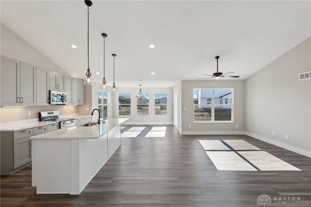 kitchen with lofted ceiling, an island with sink, gray cabinetry, a sink, and appliances with stainless steel finishes