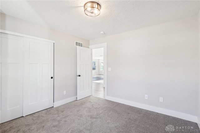 unfurnished bedroom with carpet, visible vents, baseboards, a closet, and a textured ceiling