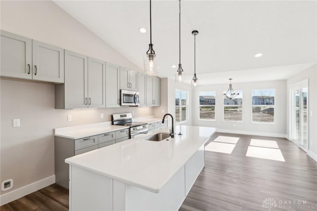kitchen featuring a center island with sink, lofted ceiling, a sink, gray cabinetry, and stainless steel appliances