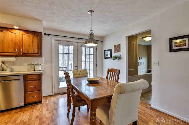 dining space with light wood-style flooring, french doors, a textured ceiling, and baseboards