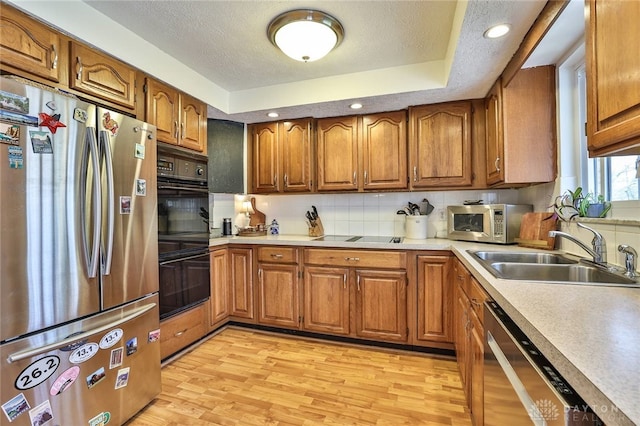 kitchen featuring light wood finished floors, black appliances, a sink, brown cabinetry, and light countertops