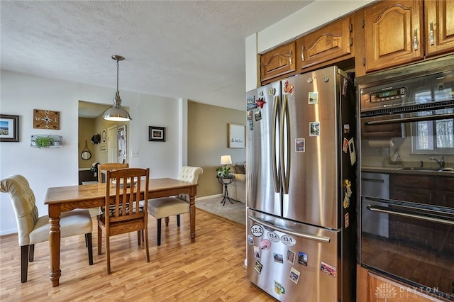 kitchen featuring a textured ceiling, brown cabinetry, light wood finished floors, freestanding refrigerator, and pendant lighting